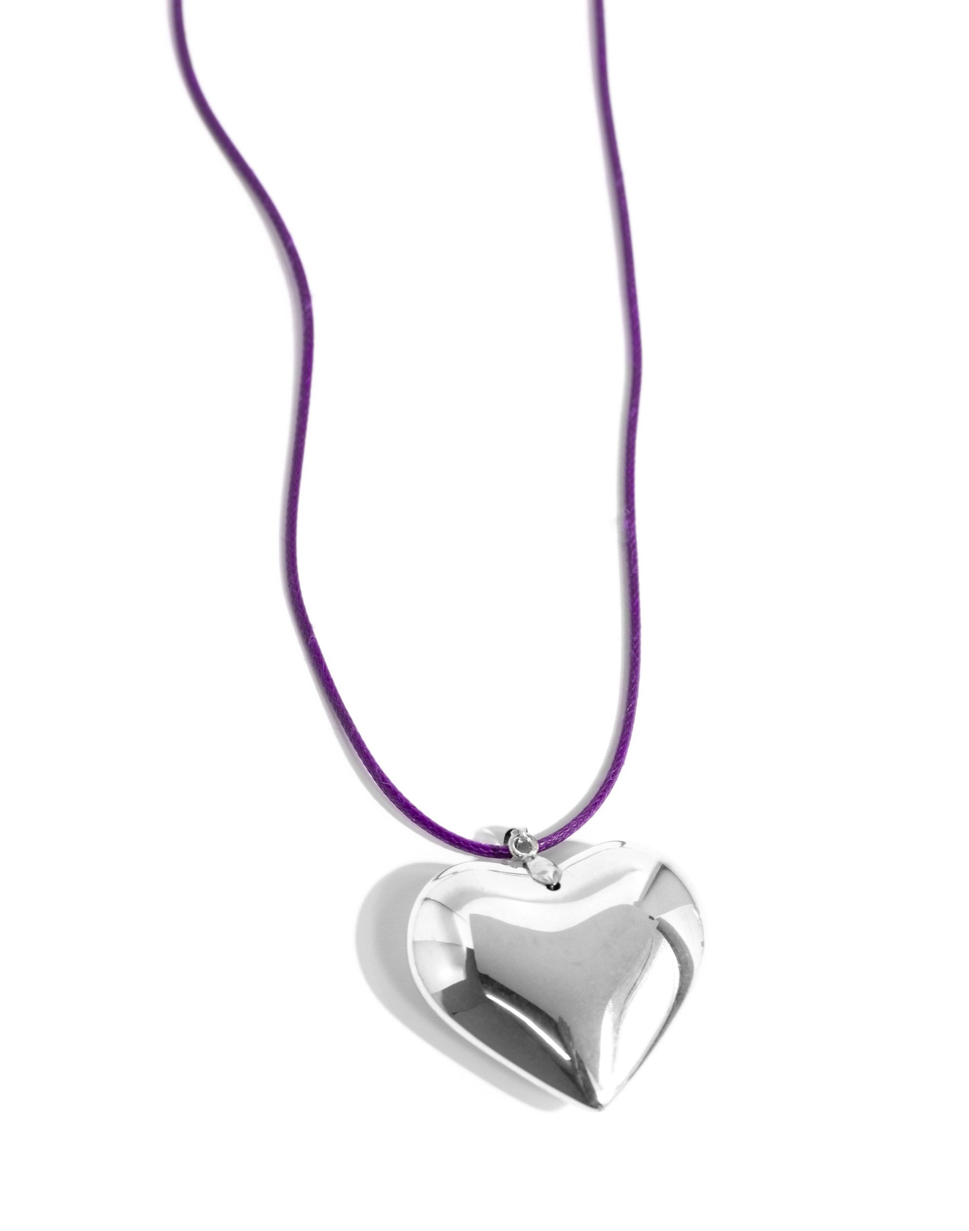 An oversized, sleek silver heart glides along a vibrant purple cord, creating a flirtatious pendant below the collar. Features an adjustable clasp closure.
N3305